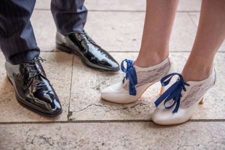 Foto de Elegantes zapatos de charol negro para hombre y zapatos de mujer blancos con cordones azules y encajes, desgastados y enfrentados entre sí. - Imagen libre de derechos