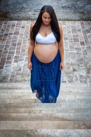 Schöne Latina Mädchen in den letzten Monaten der Schwangerschaft mit langen schwarzen Haaren eine Treppe hinauf