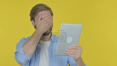 Foto de Casual Young Man Reacting to Loss on Tablet on Yellow Background - Imagen libre de derechos