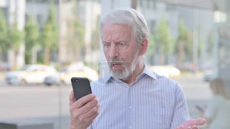 Foto de Upset Senior Old Man Reacting to Loss on Smartphone Outdoor - Imagen libre de derechos