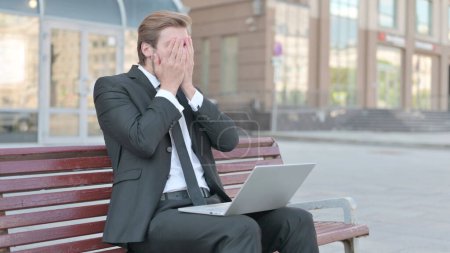 Foto de Middle Aged Businessman Reacting to Loss on Laptop while Sitting Outdoor on Bench - Imagen libre de derechos