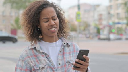 Foto de Upset Young African Woman Reacting to Loss on Smartphone Outdoor - Imagen libre de derechos