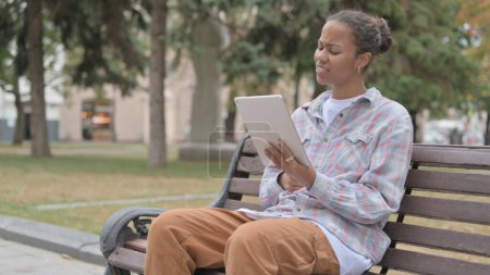 Foto de Young African Woman Reacting to Loss on Tablet while Sitting Outdoor on Bench - Imagen libre de derechos