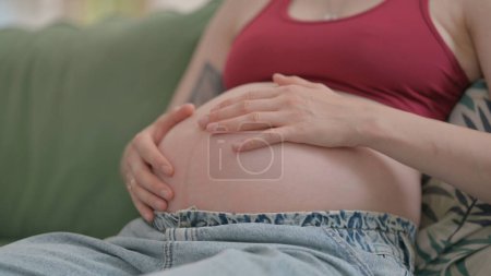 Photo for Pregnant Woman Stokes Her Big Belly while Relaxing at Home - Royalty Free Image
