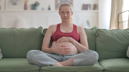 Foto de Sitting Pregnant Woman Looking at Camera while Stroking Her Tummy - Imagen libre de derechos