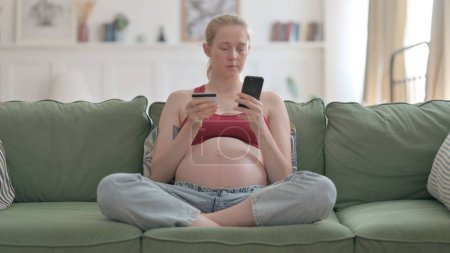 Foto de Pregnant Woman Shopping Online on Smartphone while Sitting on Sofa - Imagen libre de derechos