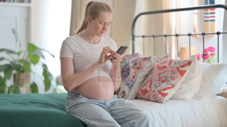 Photo for Pregnant Woman Using Smartphone while Sitting on Bed - Royalty Free Image