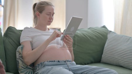 Foto de Pregnant Woman Using Tablet while Sitting at Home - Imagen libre de derechos