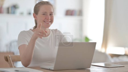 Foto de Young Woman Pointing Towards Camera while using Laptop in Office - Imagen libre de derechos