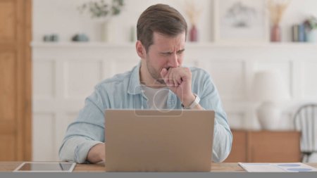 Foto de Hombre joven ocasional tosiendo mientras usa el ordenador portátil en la oficina - Imagen libre de derechos