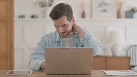 Foto de Hombre joven casual que tiene dolor de cabeza mientras trabaja en el ordenador portátil - Imagen libre de derechos