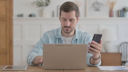 Photo for Casual Man using Smartphone while using Laptop - Royalty Free Image