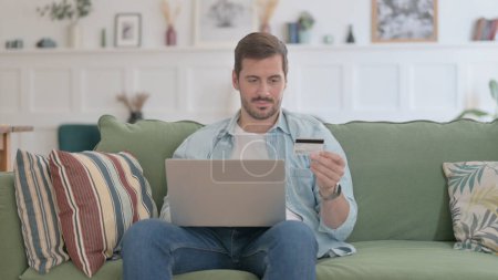 Téléchargez les photos : Casual Man making Online Payment on Laptop on Sofa - en image libre de droit