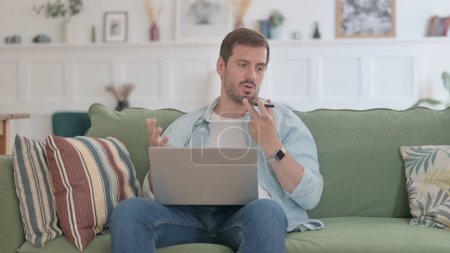 Photo for Angry Casual Man with Laptop Talking on Phone on Sofa - Royalty Free Image
