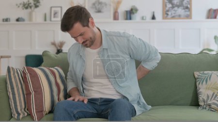 Photo for Casual Man having Neck Pain while Sitting on Sofa - Royalty Free Image