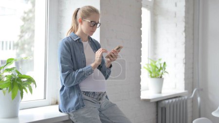 Foto de Embarazada hermosa mujer navegar por Internet en el teléfono mientras está sentado en la ventana - Imagen libre de derechos