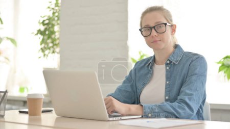 Photo for Beautiful  Woman Looking at Camera while using Laptop in Office - Royalty Free Image