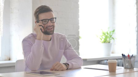Téléchargez les photos : Jeune homme adulte parlant au téléphone au bureau - en image libre de droit