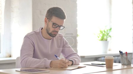 Téléchargez les photos : Jeune homme adulte écrivant sur papier au bureau - en image libre de droit
