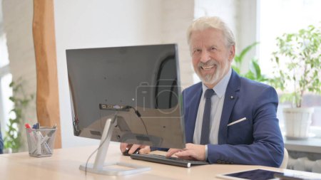 Foto de The Old Businessman Smiling at Camera while Using Desktop Computer - Imagen libre de derechos