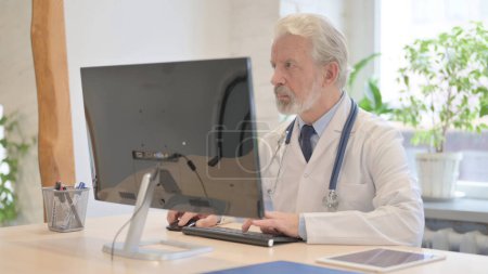 Photo for The Old Doctor Working on Laptop in Clinic - Royalty Free Image