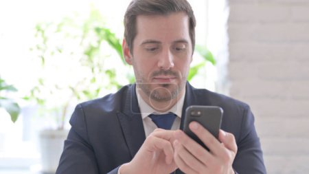 Téléchargez les photos : The Young Adult Businessman Browsing Internet on Smartphone in Office - en image libre de droit