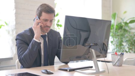 Téléchargez les photos : The Angry Young Adult Businessman Talking on Phone at Work - en image libre de droit