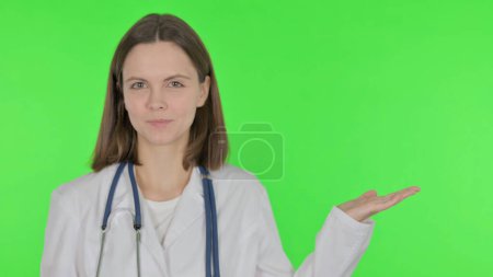 Joven doctor mostrando de lado sobre fondo verde