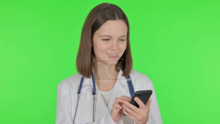 Téléchargez les photos : Jeune médecin naviguant sur Smartphone sur fond vert - en image libre de droit