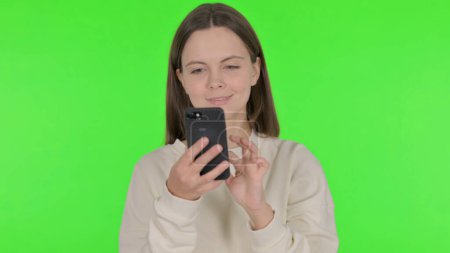 Photo for Casual Woman Browsing Smartphone on Green Background - Royalty Free Image