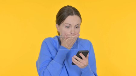 Foto de Pérdida casual de la mujer en el teléfono inteligente en el fondo amarillo - Imagen libre de derechos