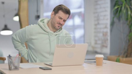 Foto de Young Adult Man having Back Pain while using Laptop - Imagen libre de derechos