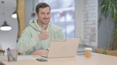 Téléchargez les photos : Thumbs Up by Young Adult Man Working on Laptop - en image libre de droit