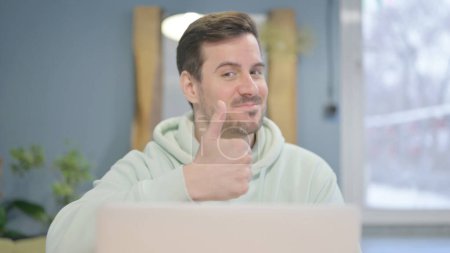 Téléchargez les photos : Close Up of Thumbs Up by Young Adult Man Working on Laptop - en image libre de droit