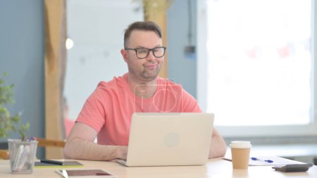 Foto de Young Adult Man Shaking Head in Rejection while Working on Laptop - Imagen libre de derechos