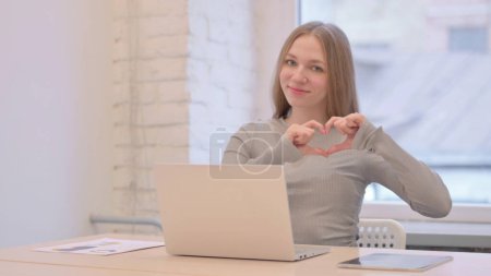 Téléchargez les photos : Creative Young Woman Showing Heart Sign while using Laptop - en image libre de droit