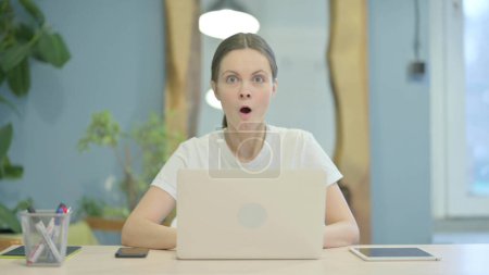 Téléchargez les photos : Shocked Young Woman Looking at Camera While Working on Laptop - en image libre de droit