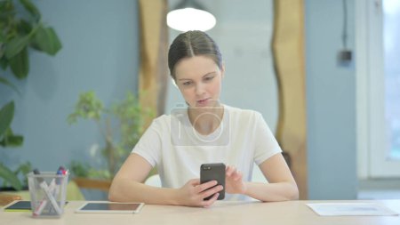 Téléchargez les photos : Young Woman Browsing Internet on Smartphone at Work - en image libre de droit