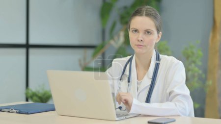 Téléchargez les photos : Jeune femme médecin regardant la caméra tout en utilisant un ordinateur portable - en image libre de droit