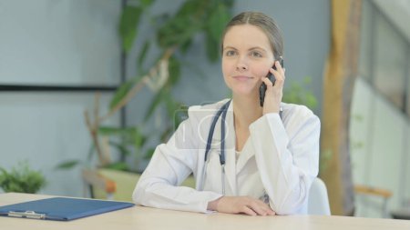 Téléchargez les photos : Jeune femme médecin parlant au téléphone à la clinique - en image libre de droit
