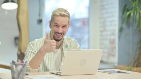 Téléchargez les photos : Pouces levées par jeune homme travaillant sur ordinateur portable - en image libre de droit