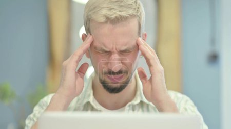 Téléchargez les photos : Gros plan sur un jeune homme souffrant de maux de tête travaillant sur un ordinateur portable - en image libre de droit