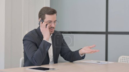 Téléchargez les photos : Homme d'affaires en colère Parler sur Smartphone au travail - en image libre de droit
