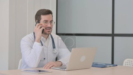 Téléchargez les photos : Docteur parlant au téléphone tout en utilisant un ordinateur portable - en image libre de droit