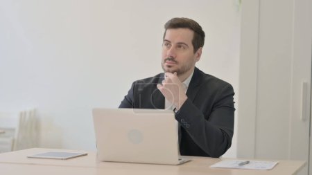 Téléchargez les photos : Homme d'affaires penser tout en travaillant sur ordinateur portable - en image libre de droit