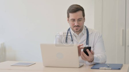 Foto de Doctor usando Smartphone mientras usa Laptop - Imagen libre de derechos