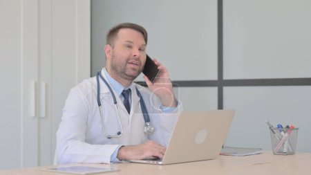 Téléchargez les photos : Jeune médecin parlant au téléphone au travail - en image libre de droit