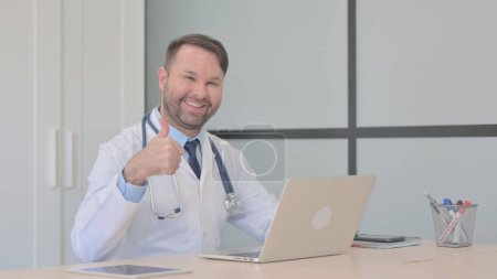Téléchargez les photos : Pouces levées par le jeune médecin sur ordinateur portable - en image libre de droit