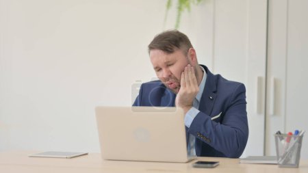 Téléchargez les photos : Homme d'affaires ayant mal aux dents tout en travaillant sur ordinateur portable, infection - en image libre de droit