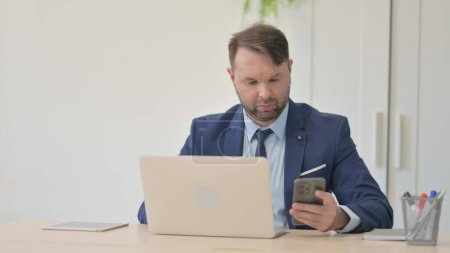 Téléchargez les photos : Homme d'affaires travaillant sur ordinateur portable et utilisant un smartphone - en image libre de droit